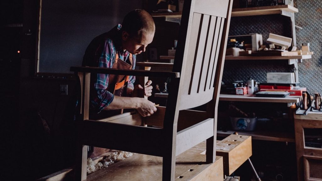 A craftsman in the process of creating a wooden chair from raw materials.